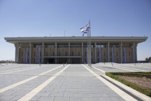 בניין הכנסת בירושלים מהכיכר הקדמית, עם שלושה דגלי ישראל מתחת לשמיים כחולים